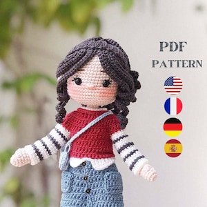 Puede incluir: Patrón de muñeca de crochet en PDF en inglés, francés, alemán y español. La muñeca lleva una camisa a rayas rojas y blancas, una falda vaquera azul y calcetines blancos con zapatos negros. La muñeca tiene el pelo castaño y la cara rosa.