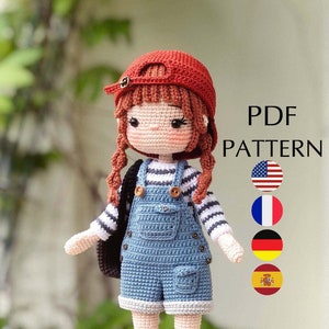 May include: Crochet doll pattern PDF in English, French, German, and Spanish. The doll is wearing a red cap, a striped shirt, blue overalls, and brown shoes. The doll has brown hair in pigtails.