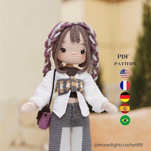 以下が含まれることがあります： 手作りの編み人形。茶色の三つ編みの髪、白いジャケット、グレーと白のパンツ、小さな紫色のバッグを着用。人形は詳細な顔をしており、PDFパターンです。「PDF PATTERN」の文字と販売者のハンドルが表示されています。