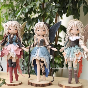 May include: Three handmade crochet dolls featuring intricate yarn hair, detailed outfits with layered petal-like skirts, and large wings. Each doll stands on a circular wooden base. The image includes text reading PDF PATTERN and @moonlighterochet89.