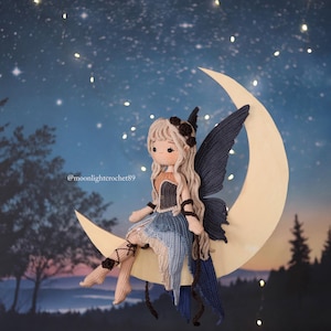 May include: A handcrafted crochet fairy doll with long blonde hair, a black floral headpiece, and blue wings sits on a crescent moon. The doll wears a blue and tan dress. The background is a night sky with stars and trees.