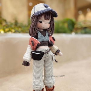 Puede incluir: Una mu&ntilde;eca de crochet con una gorra de b&eacute;isbol blanca, una chaqueta marr&oacute;n y naranja, una camiseta gris, pantalones grises y botas marrones. La mu&ntilde;eca tiene el pelo marr&oacute;n y una cara marr&oacute;n claro. La mu&ntilde;eca est&aacute; de pie sobre una superficie marr&oacute;n. @moonlightcrochet89