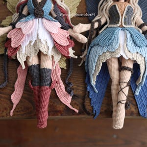 May include: Two handmade crochet fairy dolls with detailed wings and petal-like skirts. One doll features a colour palette of pinks, reds, and greens, while the other showcases blues and tans. Both dolls have long, flowing hair and are posed on a wooden surface.
