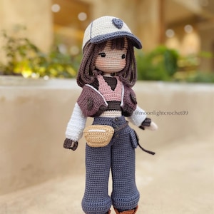 Puede incluir: Mu&ntilde;eca de crochet con una gorra de b&eacute;isbol blanca con un coraz&oacute;n, una chaqueta marr&oacute;n, un top rosa, pantalones vaqueros azules, un cintur&oacute;n marr&oacute;n y botas marrones. La mu&ntilde;eca tiene el pelo marr&oacute;n y una cara de crochet. La mu&ntilde;eca lleva una bolsa de crochet marr&oacute;n. @moonlightcrochet89