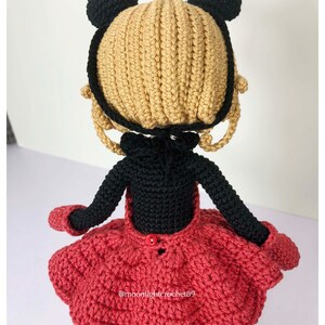 K&ouml;nnte beinhalten: Geh&auml;kelte Puppe mit schwarzen B&auml;renohren, einem schwarzen Kleid und einem roten Rock. Die Puppe tr&auml;gt einen roten Knopf auf der R&uuml;ckseite des Kleides. Die Puppe h&auml;lt ihre Arme seitlich ausgestreckt. Die Puppe steht auf einer wei&szlig;en Oberfl&auml;che. Der Text "@moonlightcrochet89" ist auf dem Rock sichtbar.