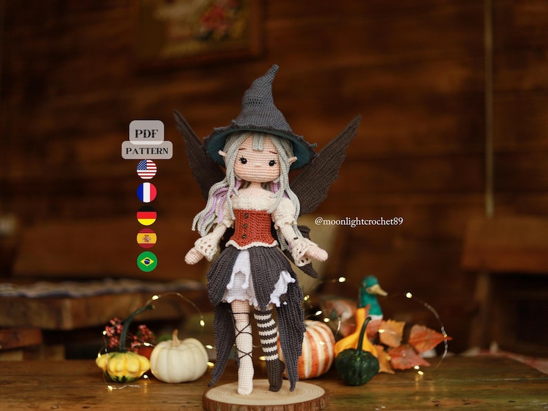 May include: A handmade crochet doll of a witch with a gray hat, wings, and a red and brown bodice. The doll has a white dress with a black skirt and striped stockings. The image includes the text "PDF PATTERN".