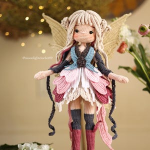 Peut inclure: Une poup&eacute;e de f&eacute;e au crochet faite &agrave; la main avec des cheveux blonds, des ailes et une robe color&eacute;e. La robe de la poup&eacute;e pr&eacute;sente des couches de rose, de blanc et de bordeaux. La poup&eacute;e est pos&eacute;e sur une tranche de bois. Le compte Instagram du cr&eacute;ateur de la poup&eacute;e est @moonlightcrochet89.