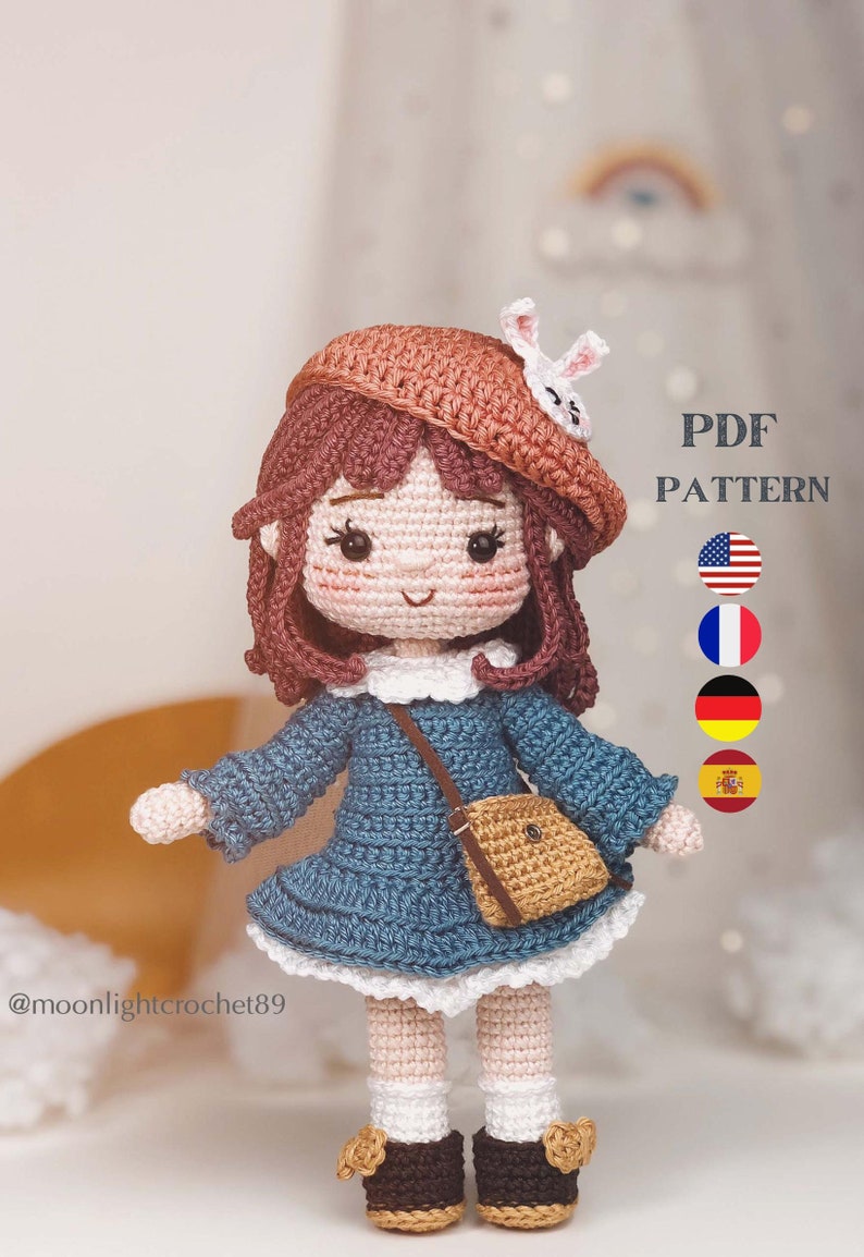May include: Crochet doll pattern in PDF format. The doll is wearing a blue dress, brown shoes, a brown hat, and a brown bag. The pattern is available in English, French, German, and Spanish.