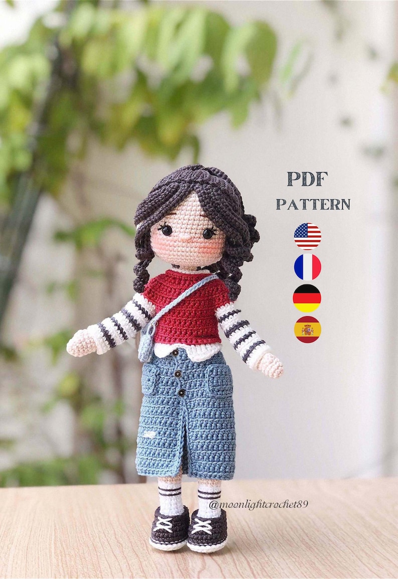 May include: Crochet doll pattern PDF in English, French, German, and Spanish. The doll is wearing a red and white striped shirt, a blue denim skirt, and white socks with black shoes. The doll has brown hair and a pink face.