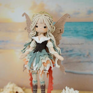 Puede incluir: Una mu&ntilde;eca de ganchillo hecha a mano con pelo largo rubio, orejas puntiagudas y grandes ojos marrones. La mu&ntilde;eca lleva un vestido de capas en tonos blanco, marr&oacute;n, azul verdoso y naranja, con alas a juego y botas de color marr&oacute;n oscuro.