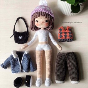 May include: Crocheted doll with brown hair wearing a purple and white hat, white shirt, white shorts, and brown trousers. The doll is holding a black handbag. The doll is surrounded by other crocheted clothing items, including a blue jacket, a brown waistcoat, and a pair of brown shoes. The image includes the text "@moonlightcrochet89".