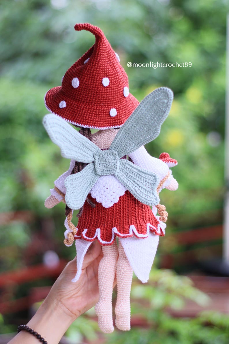 May include: A handmade crochet doll with a red mushroom cap with white spots, a red dress, and light blue wings. The doll has a whimsical fairy design. The text "@moonlightcrochet89" is visible on the image.
