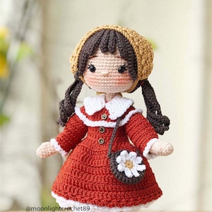May include: A crocheted doll with brown hair, wearing a red dress, a white collar, a brown purse with a white flower, and a brown and yellow hat. The doll is wearing white and brown striped socks.