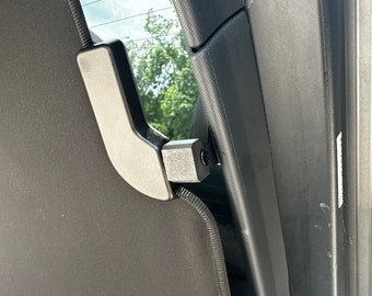 May include: A black fabric car window shade with a black plastic handle and a metal latch. The shade is partially open and the handle is visible.