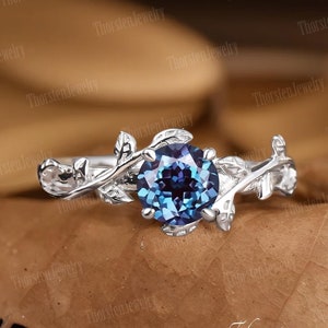 Könnte beinhalten: Ein silberner Ring mit einem blauen Edelstein, der in einem zarten Rankendesign gefasst ist. Der Ring liegt auf einem braunen Hintergrund.