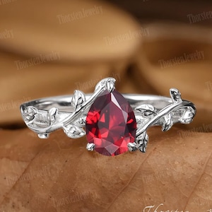 Puede incluir: Un anillo de plata con una piedra roja en forma de pera y un diseño de vid con hojas.
