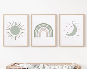 May include: Three framed art prints featuring a sun, rainbow, and moon with stars. The sun is light green with pink and green rays. The rainbow has green, pink, and white arches. The moon is light green with pink and green stars. The frames are light brown.