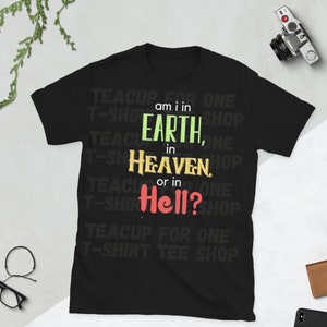 May include: Black t-shirt with the text "TEACUP FOR ONE T-SHIRT TEE SHOP" repeated around the design. The text "am i in EARTH, in HEAVEN, or in Hell?" is in the center of the shirt in a colorful font.