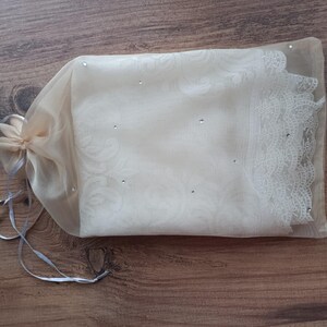 May include: A white sheer fabric bag with a lace trim and small rhinestones. The bag is tied with a white ribbon.