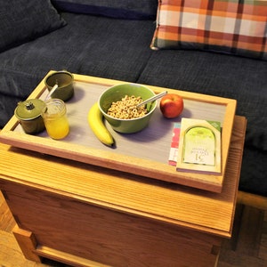 May include: A wooden tray with a light gray surface sits on a wooden table. The tray holds a bowl of cereal, a banana, an apple, a glass of orange juice, a small jar with a lid, and a book titled "31 Days of Prayer".