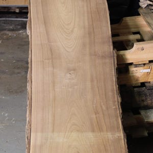 May include: A large, light brown wood slab with a live edge. The wood has a natural grain pattern and is smooth to the touch.