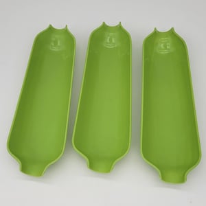 May include: Three bright green plastic corn holders. Each holder is shaped like a corn cob, with a rounded base and a flared top. The holders are empty and arranged on a white surface.