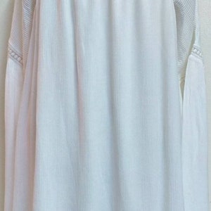 May include: White, long-sleeved, lightweight blouse with a tie at the neckline and bell sleeves.