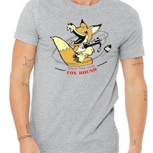 May include: A gray t-shirt with a cartoon fox holding a gun. The fox is wearing a red bandana and has a red nose. The text "Special Force Group FOX HOUND" is printed below the fox.
