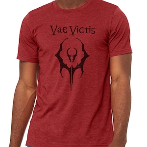 May include: A red heather t-shirt with a black graphic design of a stylized symbol and the text "Vae Victis".