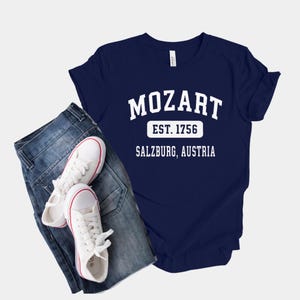 May include: A navy blue t-shirt with white text that reads "Mozart Est. 1756 Salzburg, Austria".