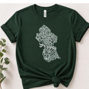 May include: A dark forest green short-sleeve t-shirt featuring a white graphic of the map of Guyana filled with intricate mandala-style floral patterns. The word Guyana is written in a white cursive script across the center of the map design.