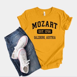 May include: A yellow t-shirt with black text that reads "Mozart Est. 1756 Salzburg, Austria".