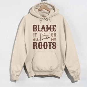 May include: A beige hoodie with a brown graphic that says "Blame it all on my roots" with a silhouette of the state of Connecticut inside the word "home".