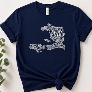 Puede incluir: Una camiseta azul marino de manga corta con un gráfico blanco del mapa de Haití relleno de intrincados patrones de estilo mandala. La palabra Haiti está escrita en una tipografía cursiva blanca en el centro del diseño sobre el pecho.