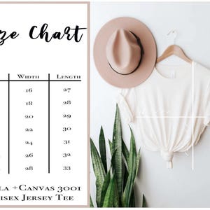 Op de afbeelding: Een wit Bella+Canvas 3001 unisex jersey t-shirt weergegeven met een maattabel met breedtes en lengtes in inches voor de maten XS tot 3XL. Het shirt hangt aan een hanger naast een beige hoed en een groene plant, met witte lijnen voor de afmetingen.