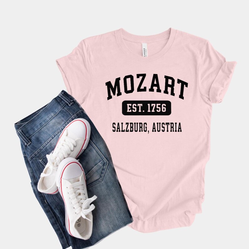 May include: Pink t-shirt with black text that reads "Mozart Est. 1756 Salzburg, Austria".