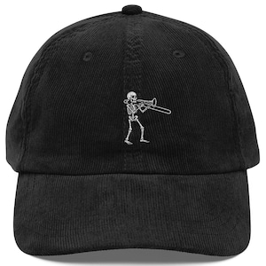 Puede incluir: Una gorra de béisbol de pana negra con un bordado blanco que muestra un esqueleto tocando el trombón. La gorra tiene una corona estructurada, una visera curva y un botón en la parte superior, con la ilustración del esqueleto centrada al frente.