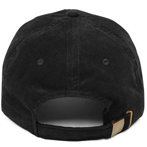 May include: A black corduroy baseball cap featuring a six-panel construction with stitched eyelets on each panel. The back of the cap includes an adjustable fabric strap with a metallic gold-toned buckle closure for a secure and customizable fit.