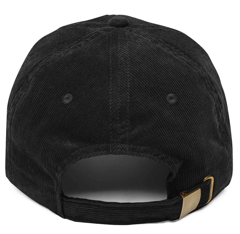 May include: A black corduroy baseball cap featuring a six-panel construction with stitched eyelets on each panel. The back of the cap includes an adjustable fabric strap with a metallic gold-toned buckle closure for a secure and customizable fit.