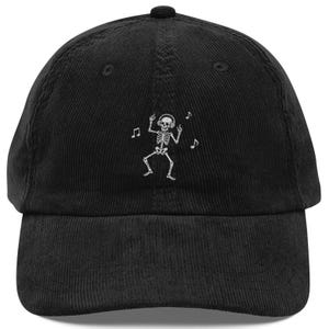 Peut inclure: Une casquette de baseball en velours côtelé noir avec une broderie blanche représentant un squelette portant un casque audio et dansant, entouré de petites notes de musique. La casquette possède une calotte structurée et une visière courbée.