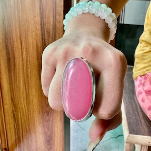 Puede incluir: Un anillo ovalado grande con una piedra rosa engastada en una banda plateada.