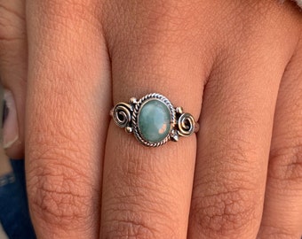 May include: A silver ring with a green oval gemstone set in a decorative silver band. The band features intricate swirls and details.