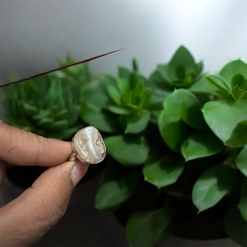 May include: A silver ring with a large, white, irregular shaped pearl. The pearl has a natural, organic look.