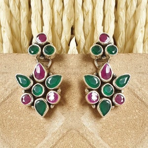 Könnte beinhalten: Ein Paar silberne Ohrringe mit grünen und rosafarbenen Edelsteinen. Die Ohrringe haben die Form einer Blume mit mehreren Blütenblättern.