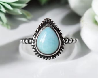 May include: A silver ring featuring a teardrop-shaped blue gemstone set in an ornate silver bezel.