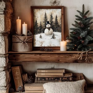 May include: A rustic wooden shelf with a framed painting of a snowman in a winter forest, two lit candles, a small artificial pine tree, and a stack of books.
