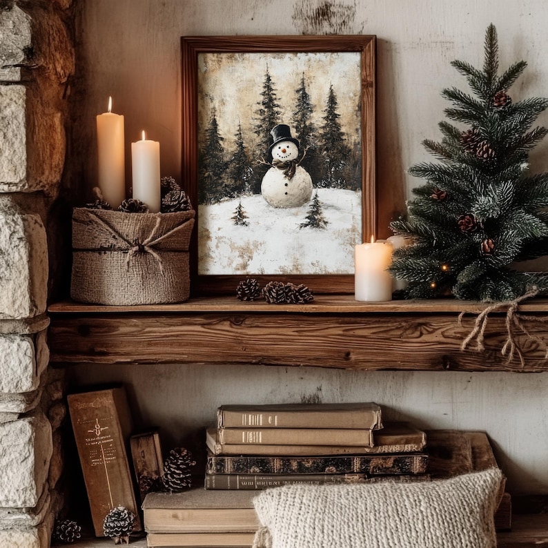 May include: A rustic wooden shelf with a framed painting of a snowman in a winter forest, two lit candles, a small artificial pine tree, and a stack of books.