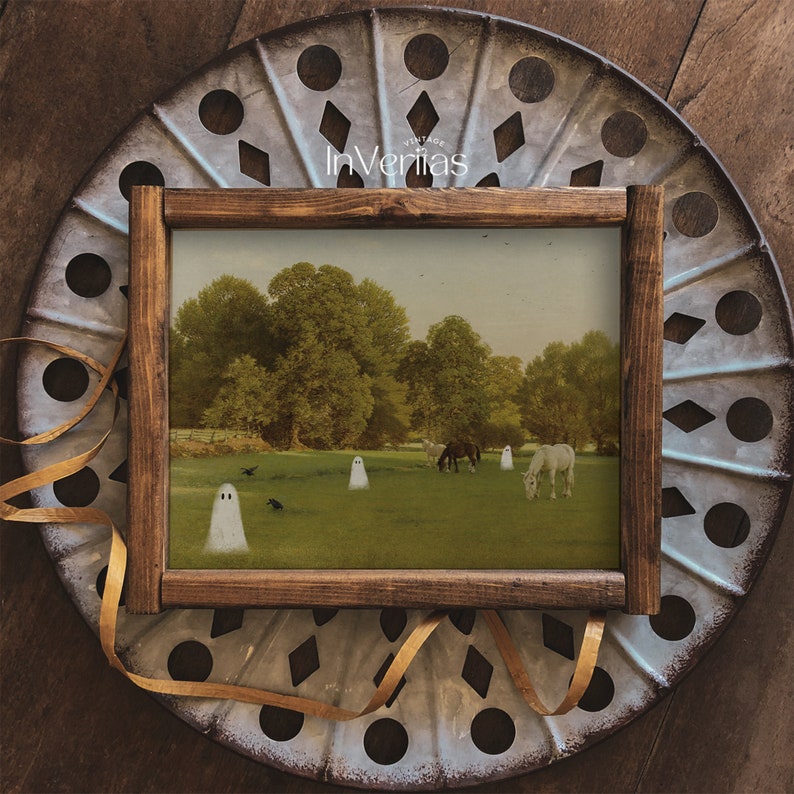 May include: A framed print featuring a pastoral scene with horses grazing in a field, with ghostly figures and crows. The wooden frame surrounds the artwork, set against a decorative metal background. The text "Vintage InVeritas" is visible.