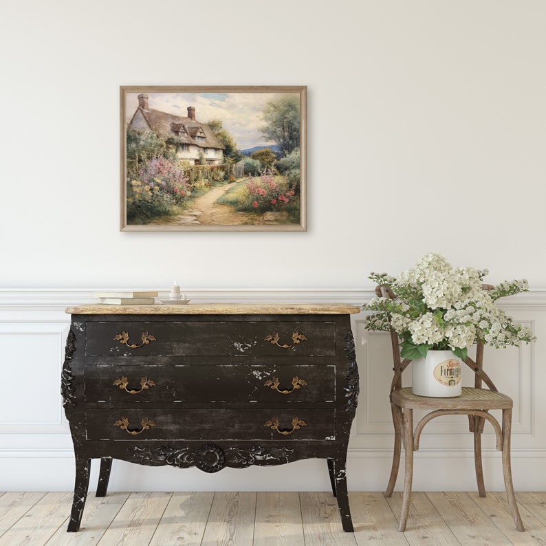 May include: A watercolor painting of a cottage with a thatched roof and a garden in front of it. The cottage is surrounded by lush greenery and flowers. The painting is framed in a light wood frame.