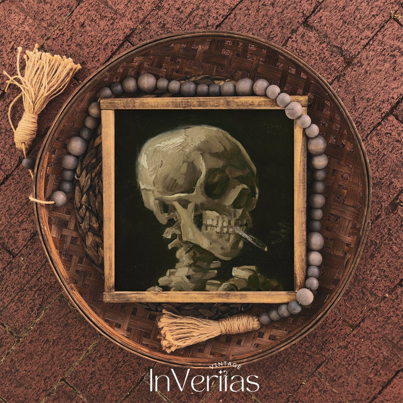 May include: A framed painting of a human skull with a cigarette in its mouth. The painting is set against a dark background and is surrounded by a wooden frame. The painting is displayed on a woven tray with a beaded garland.